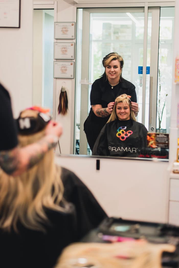 Britt Bishop smiling in the mirror while adding extensions to a client's hair